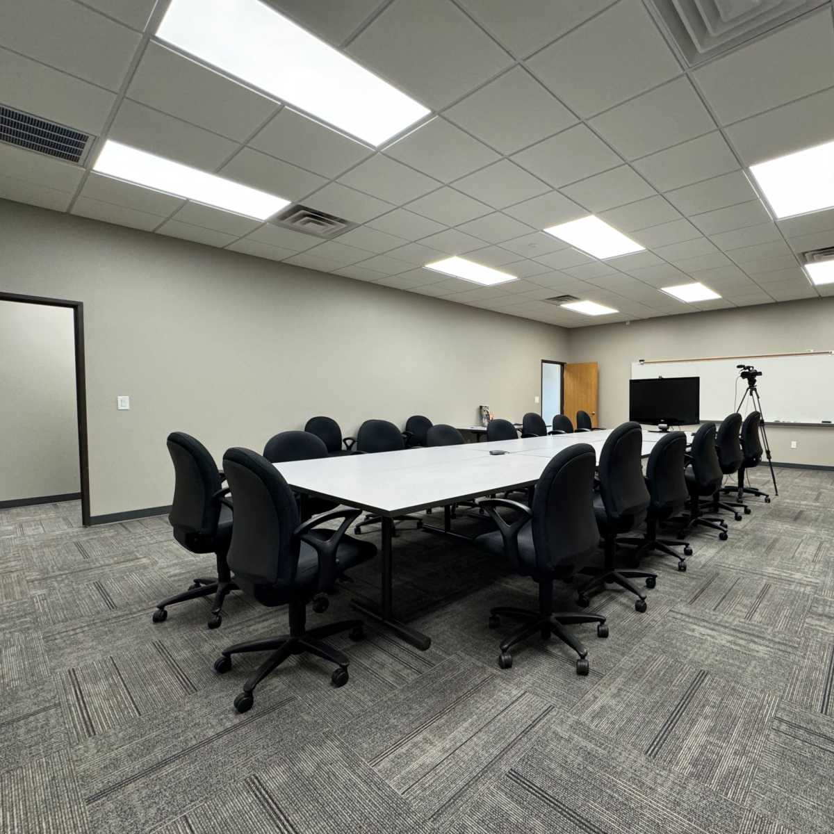 A large conference room with a rectangular table surrounded by office chairs, and a projection screen on one wall.