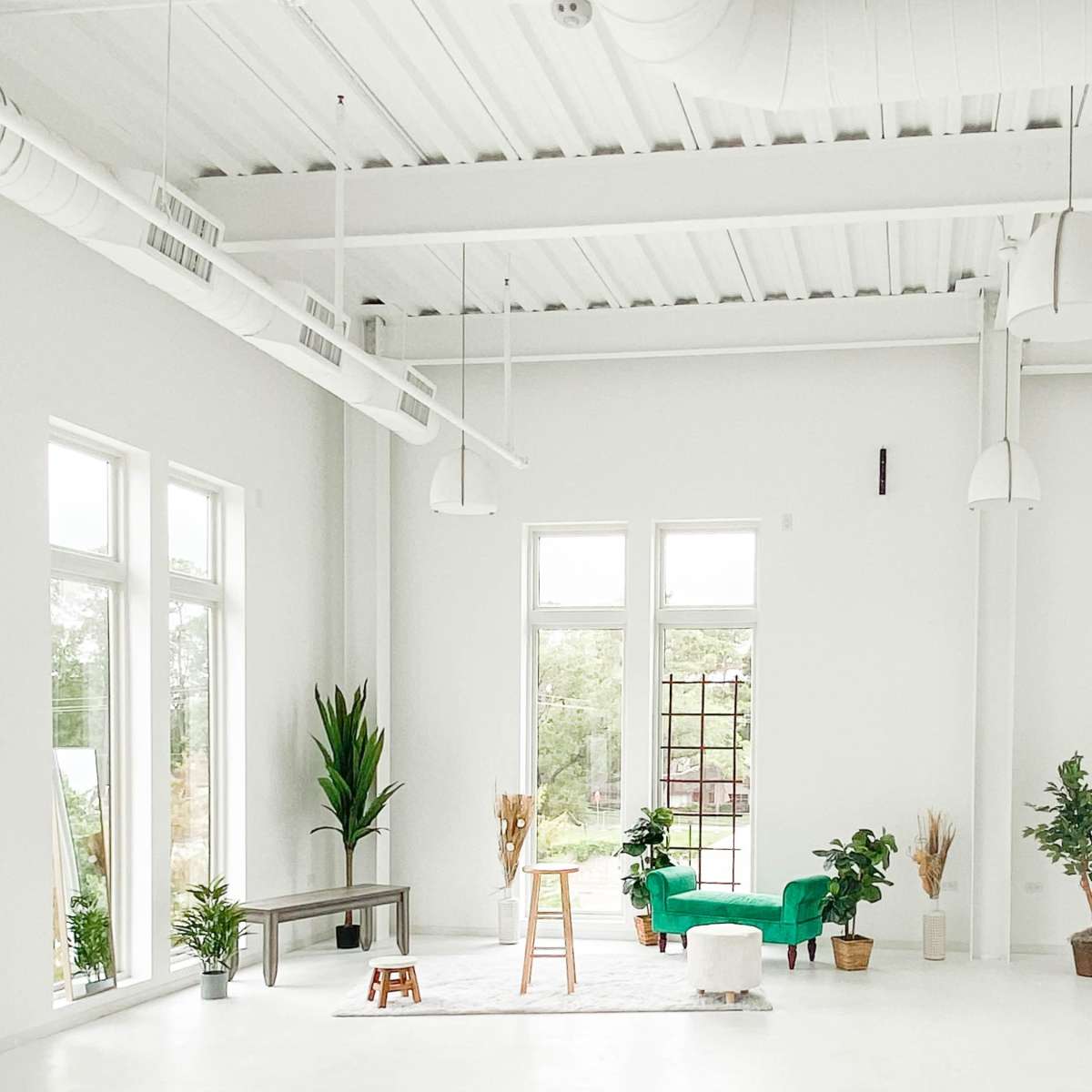A spacious, bright room with large windows, plants, a stool, and minimalist furniture.