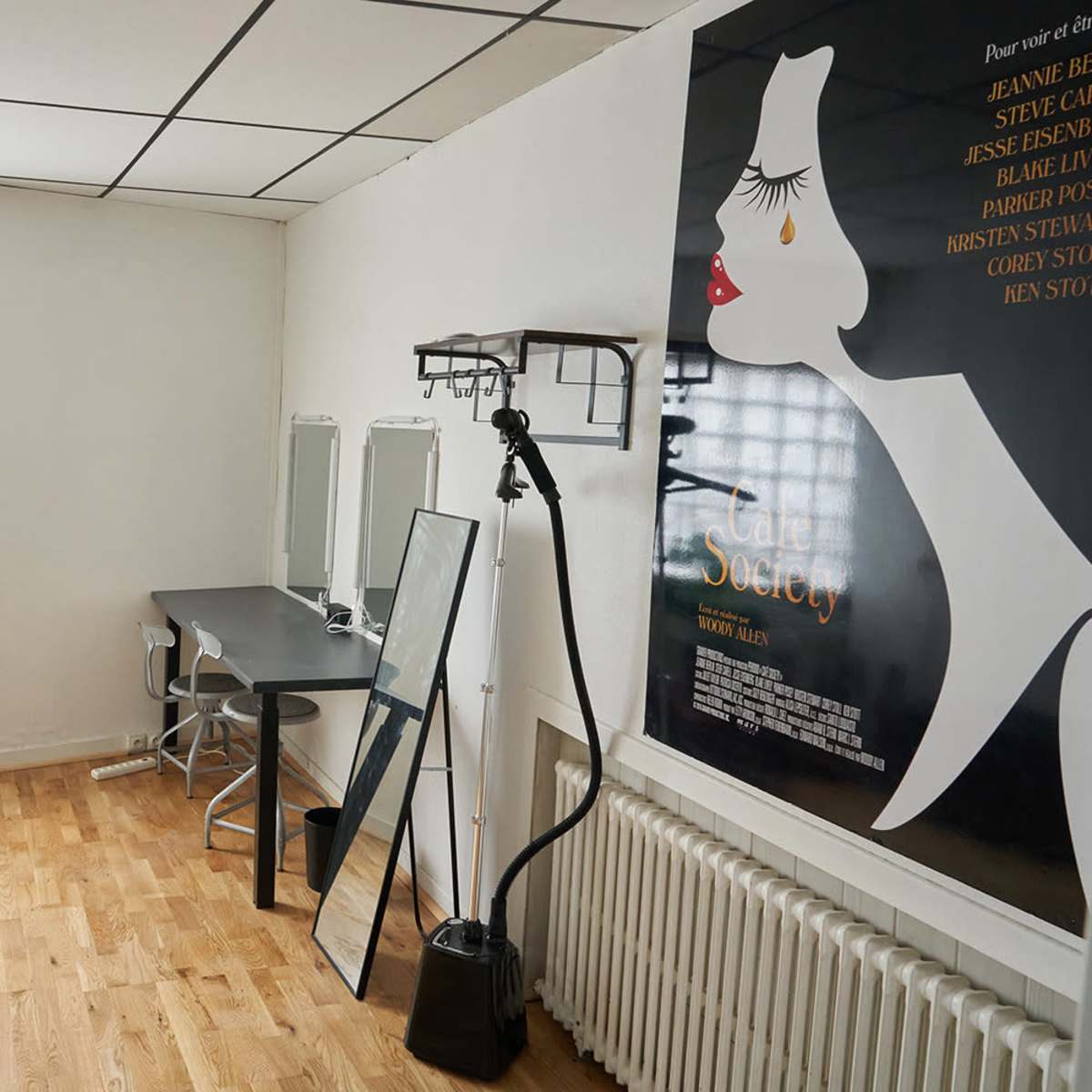 A bright room featuring a desk with a chair, a large mirror, a potted plant, and a film poster on the wall.