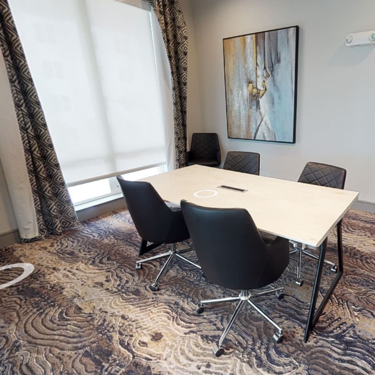 A small conference room features a rectangular table with four black chairs and an abstract artwork on the wall.