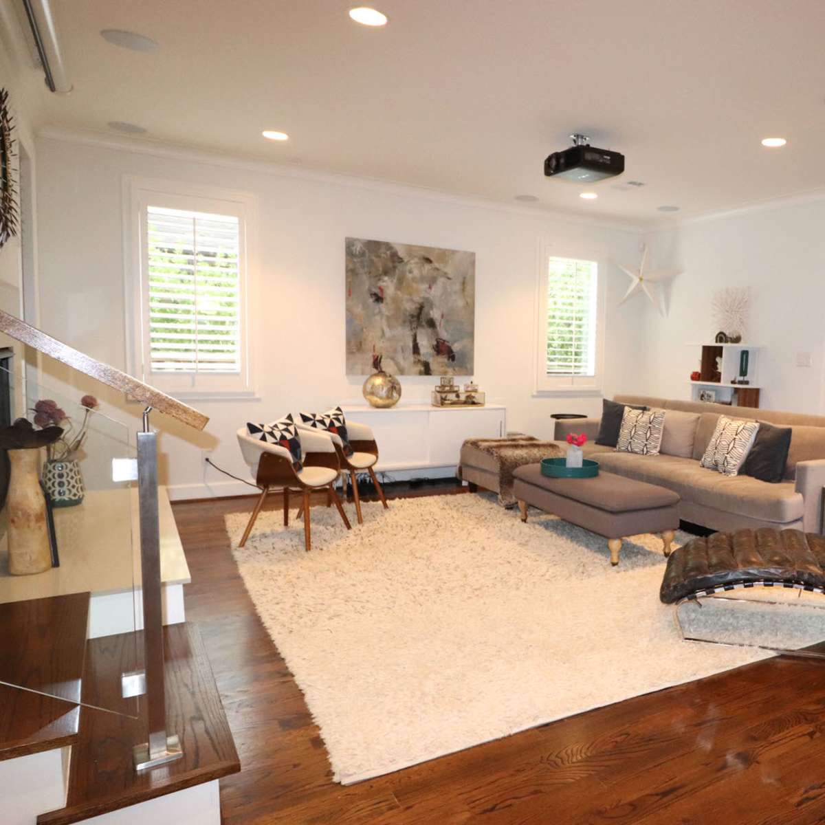 A modern living room features a sectional sofa, a sleek lounge chair, a large area rug, and glass doors leading to an outdoor space.