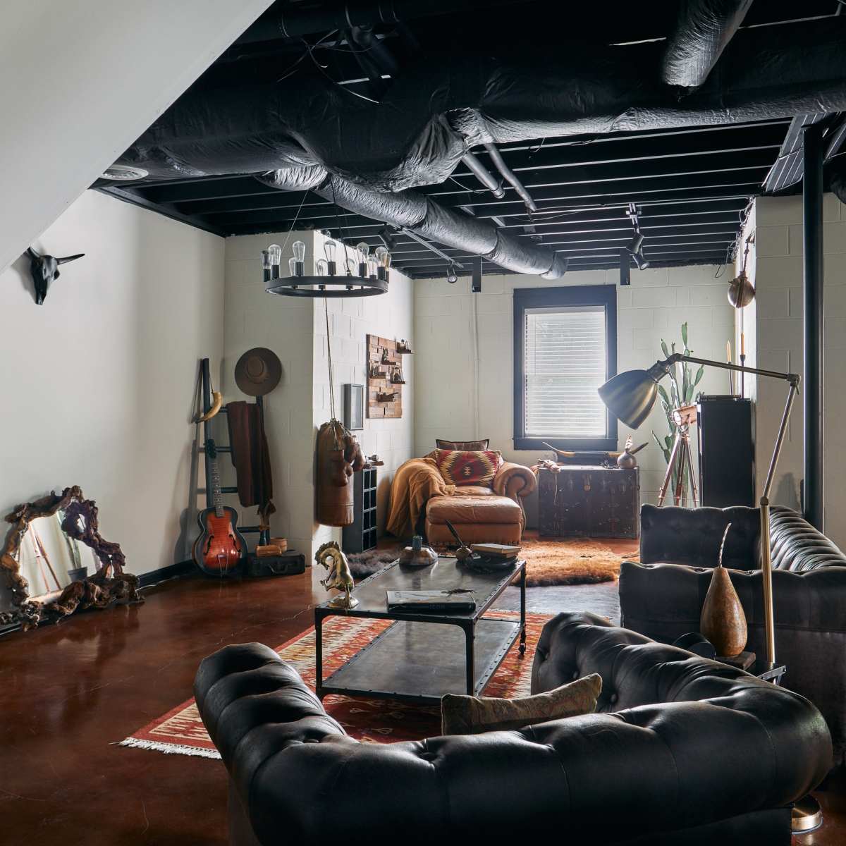 A spacious living room featuring dark leather sofas, a large coffee table, various decorative items, and a combination of industrial and vintage decor elements.
