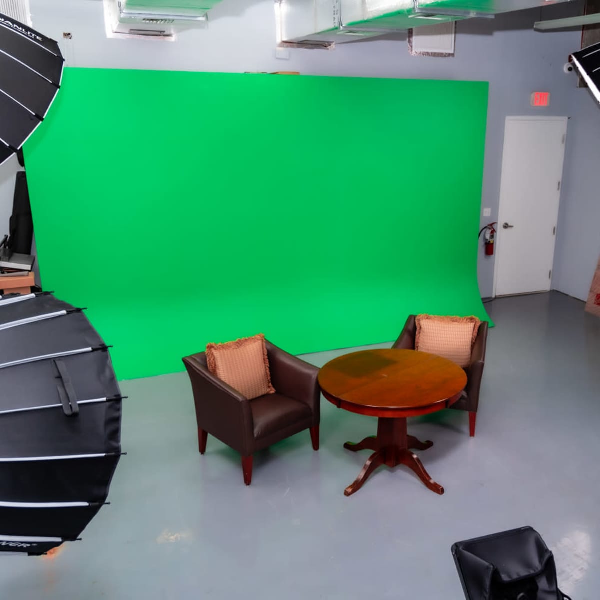 A green screen studio setup features two chairs and a round table, surrounded by studio lights and equipment.