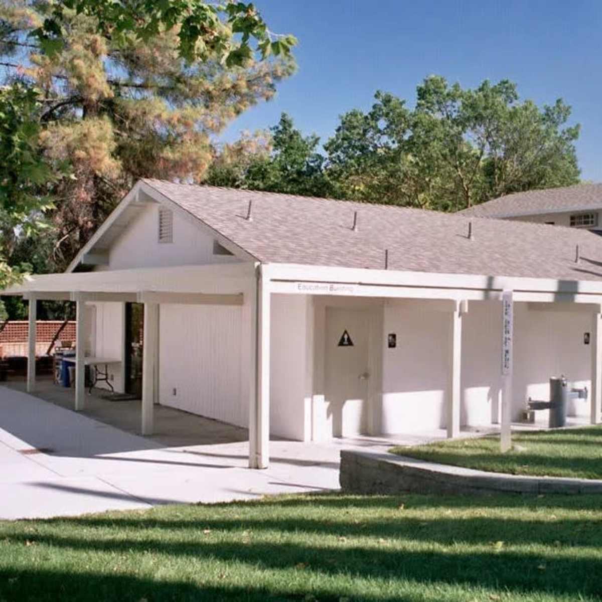 A two-story, white building with a sloped roof surrounded by green grass and trees.
