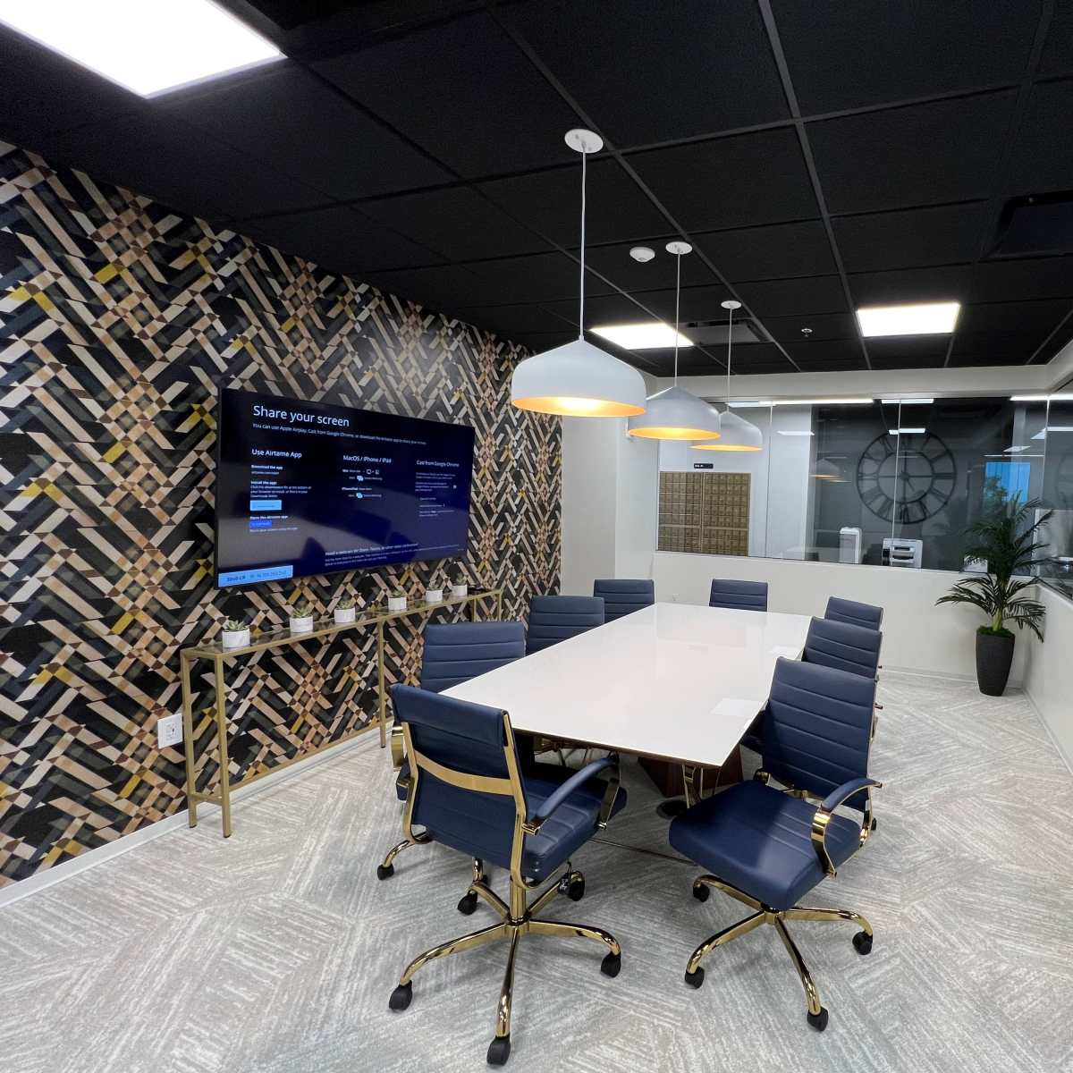 A modern conference room with a large white table surrounded by blue chairs, a large wall-mounted screen, and a patterned accent wall.