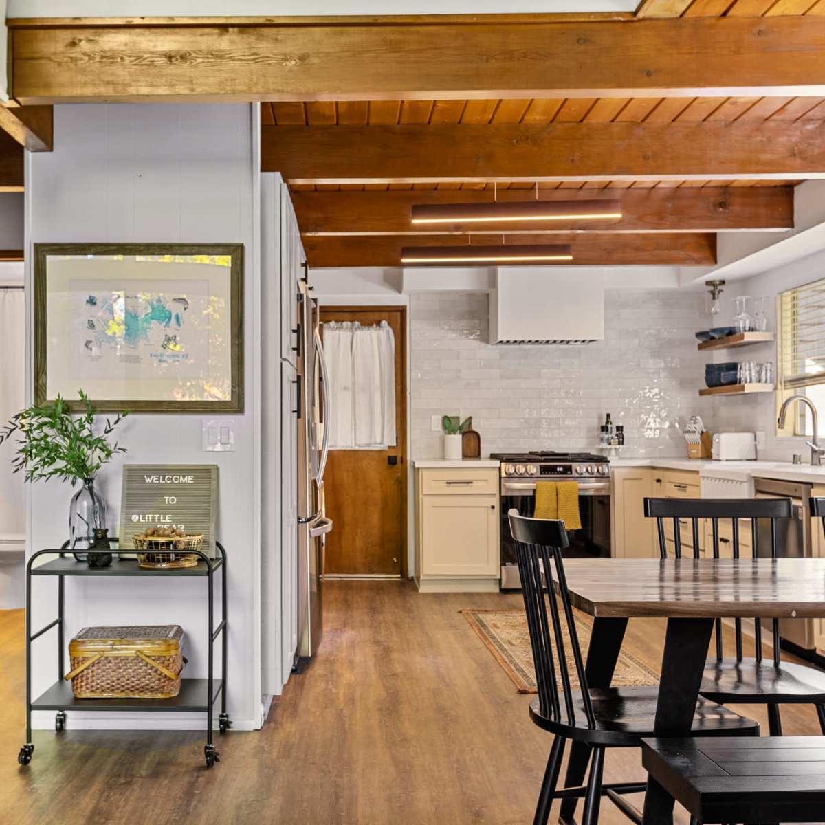 A modern kitchen and dining area with wooden beams, cabinetry, and a table set for meals.