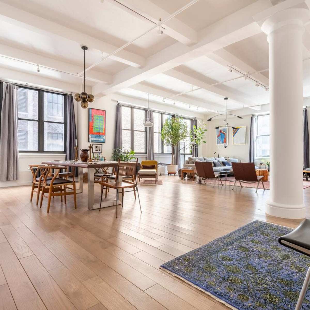 A spacious, modern interior with wooden floors, large windows, and a mix of dining and living areas furnished with various seats and decorative elements.