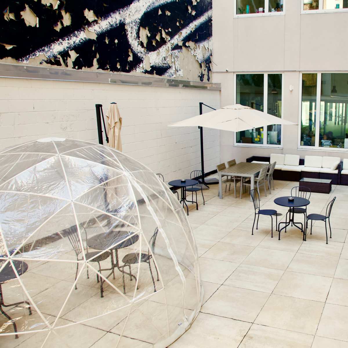 A modern outdoor lounge area featuring a clear dome structure, several seating arrangements, and a large umbrella.