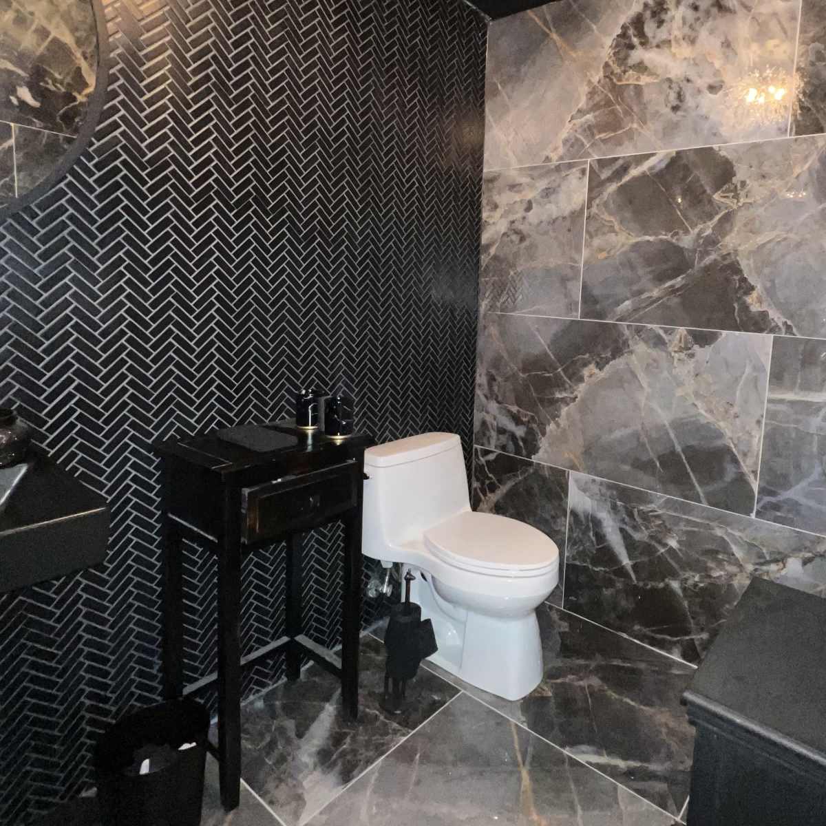 A modern bathroom featuring a white toilet, a black vanity table, and walls adorned with large, dark marble tiles.