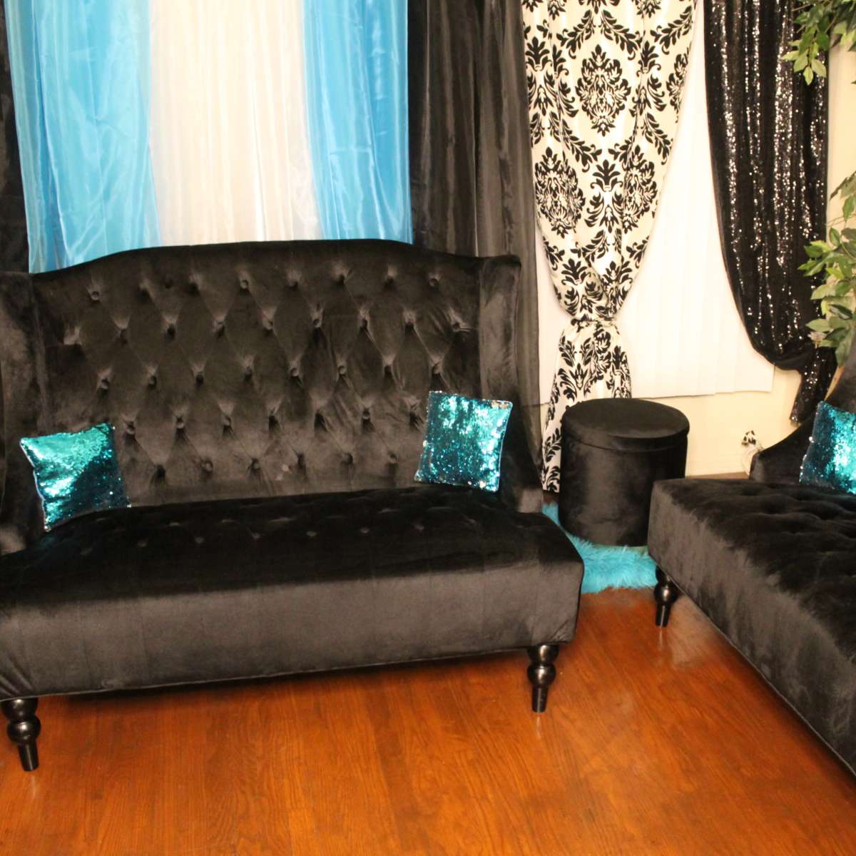 A living room with two black velvet sofas, each featuring turquoise sequin pillows, set against a backdrop of black and turquoise drapes and patterned curtains.