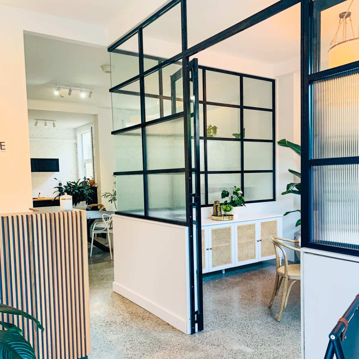 A modern interior space featuring a glass partition, plants, and a polished concrete floor.