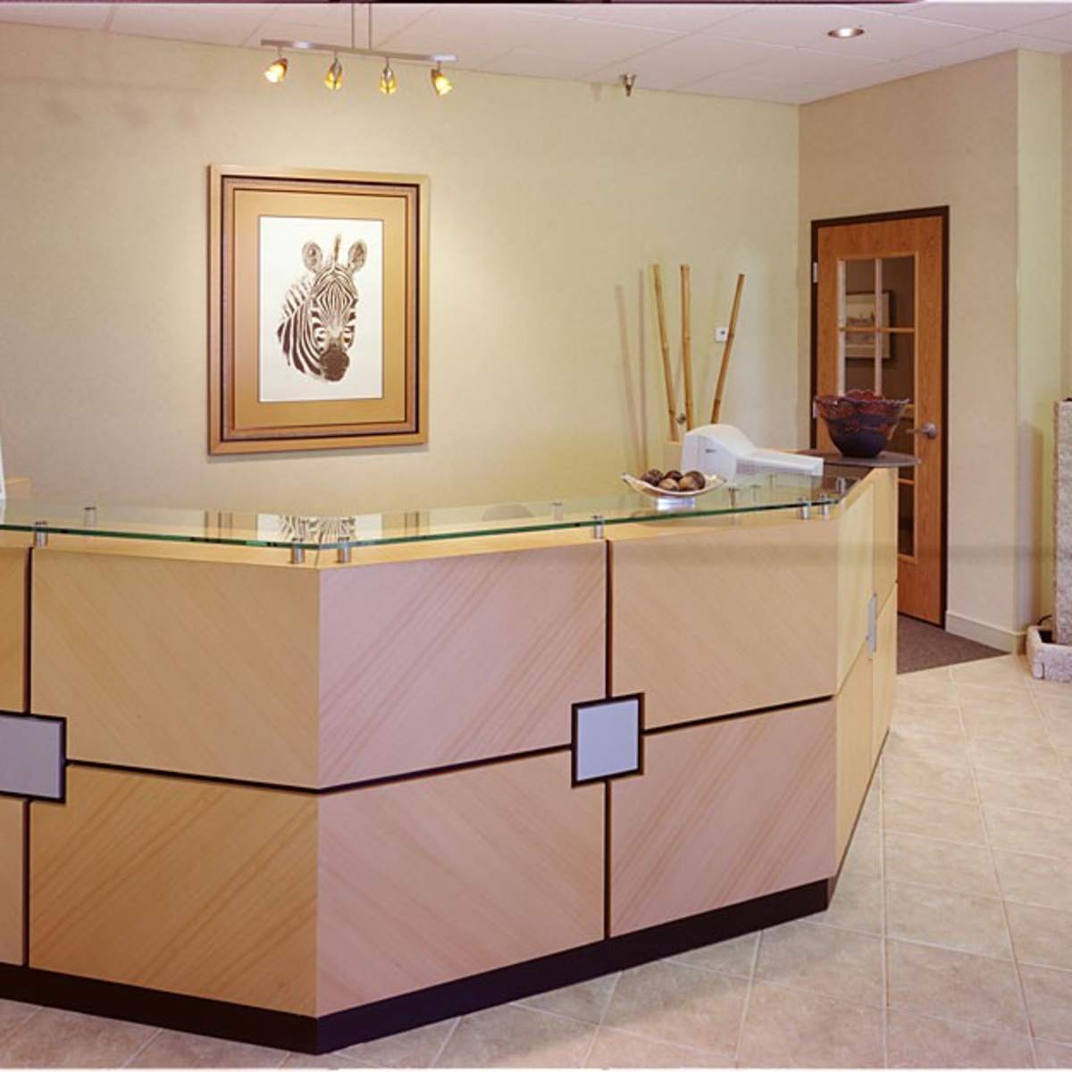 A reception area with a wooden front desk, a zebra artwork on the wall, and potted plants in the corner.
