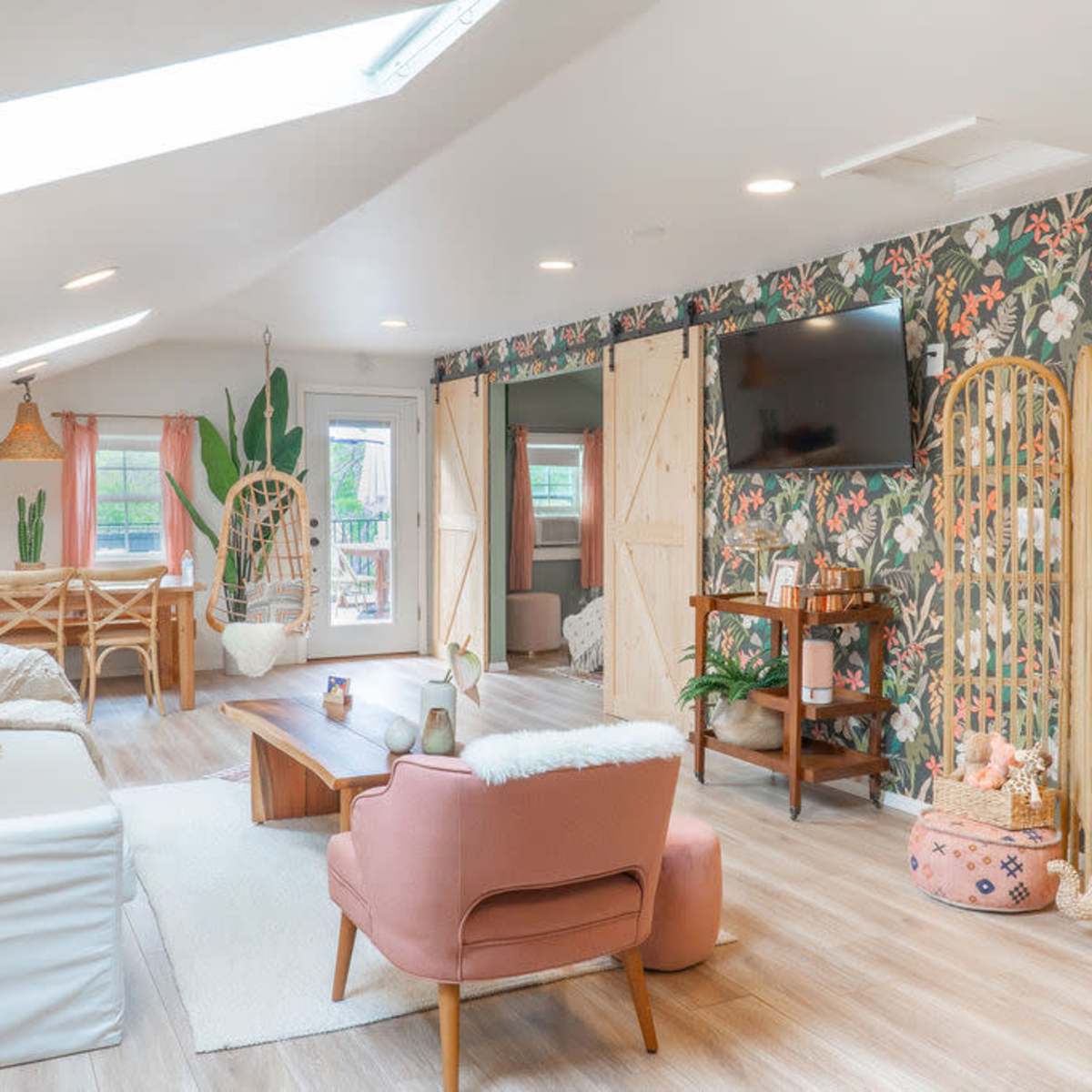 A bright, open living space featuring floral wallpaper, a dining area, and various seating options, including a pink armchair and a white sofa.