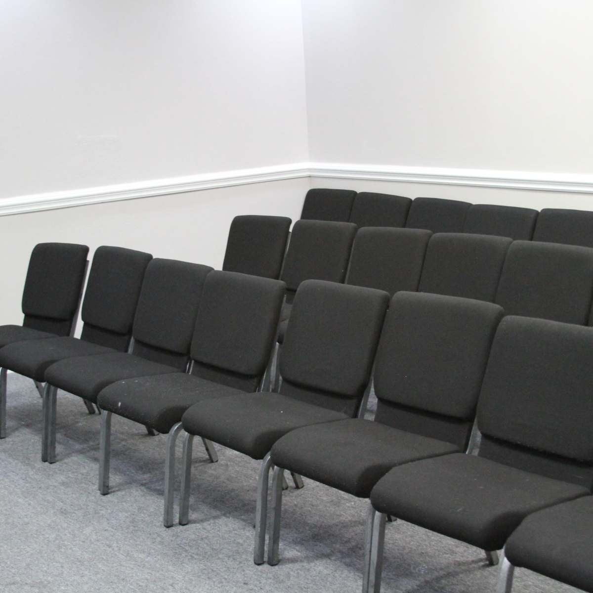 A row of black chairs arranged neatly on a gray carpet in a plain room.