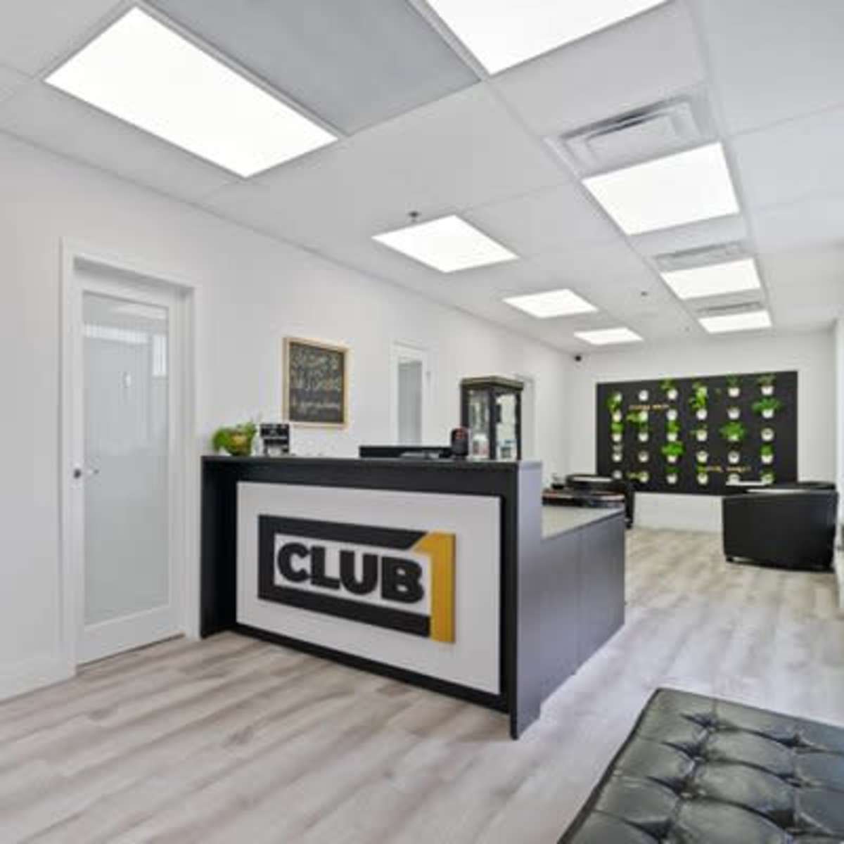 A modern office reception area with a black front desk labeled "CLUB 1" and sleek, white walls.