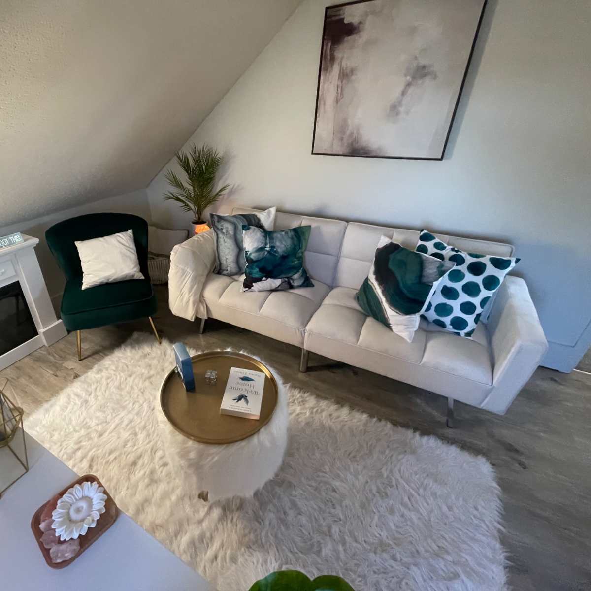 A modern living room features a sectional sofa with decorative cushions, a round coffee table on a plush rug, and a small electric fireplace.