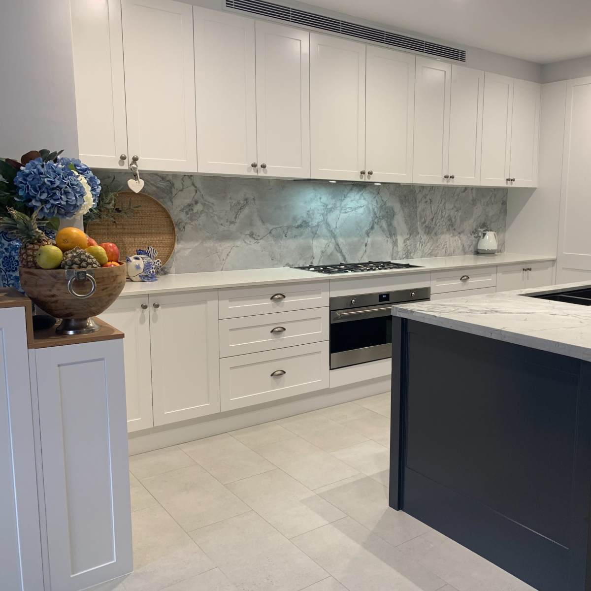 The kitchen features white cabinetry, a marble backsplash, a central island with a marble countertop, and wooden stools lined up in front.