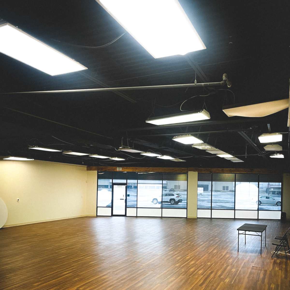 A spacious, empty room with wooden flooring and large windows allowing light to enter.