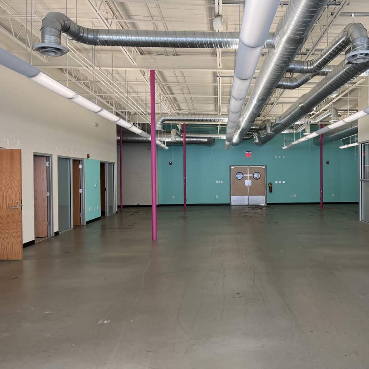 An empty commercial space with concrete flooring, large windows, and exposed ductwork on the ceiling.