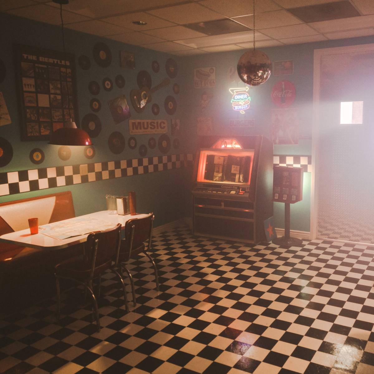 A retro diner with checkered flooring, vinyl seating, and vintage music decor on the walls.