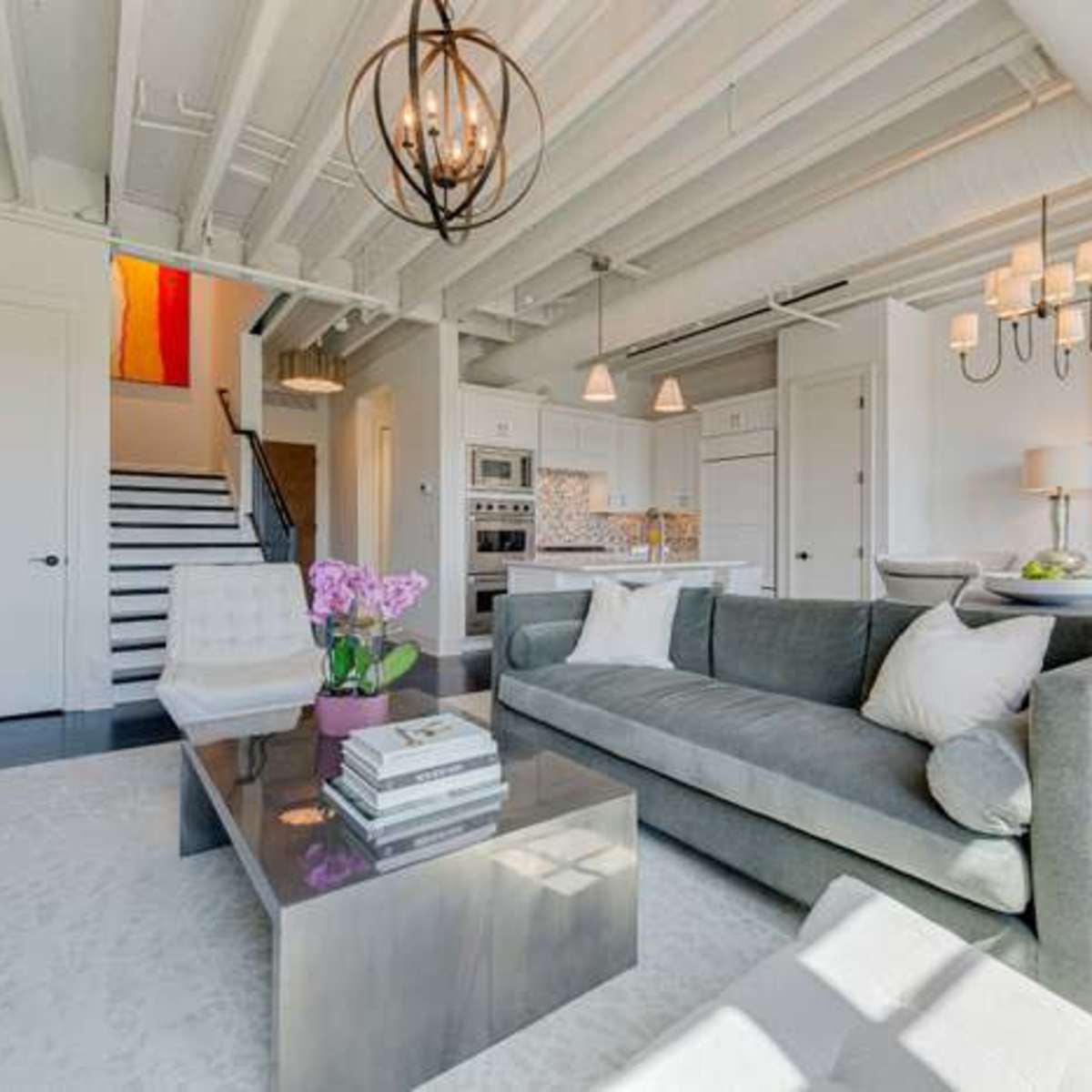 A modern living room featuring a gray sofa, a glass coffee table, and a staircase leading to another level.