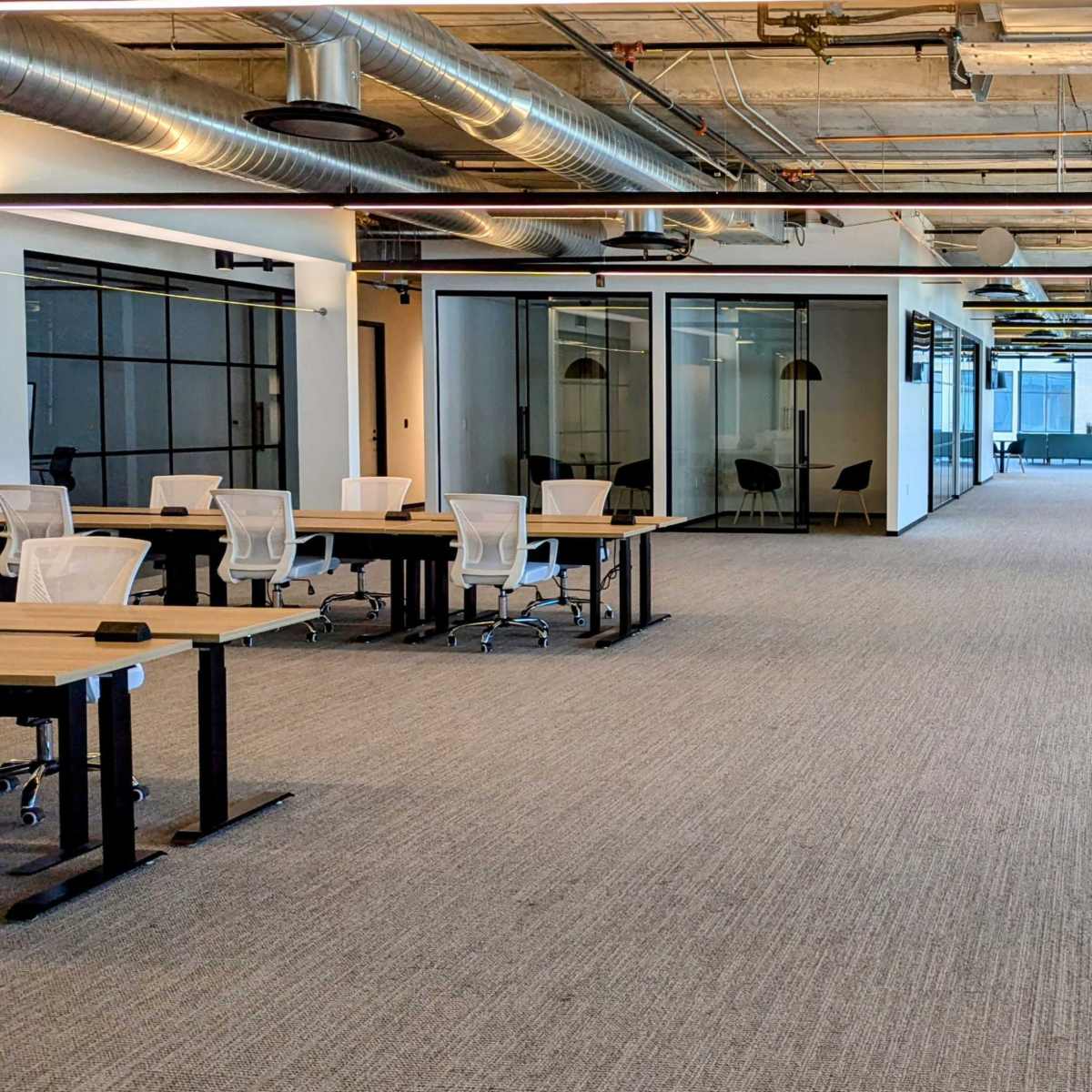 A spacious open office layout with empty desks and large windows allowing natural light.