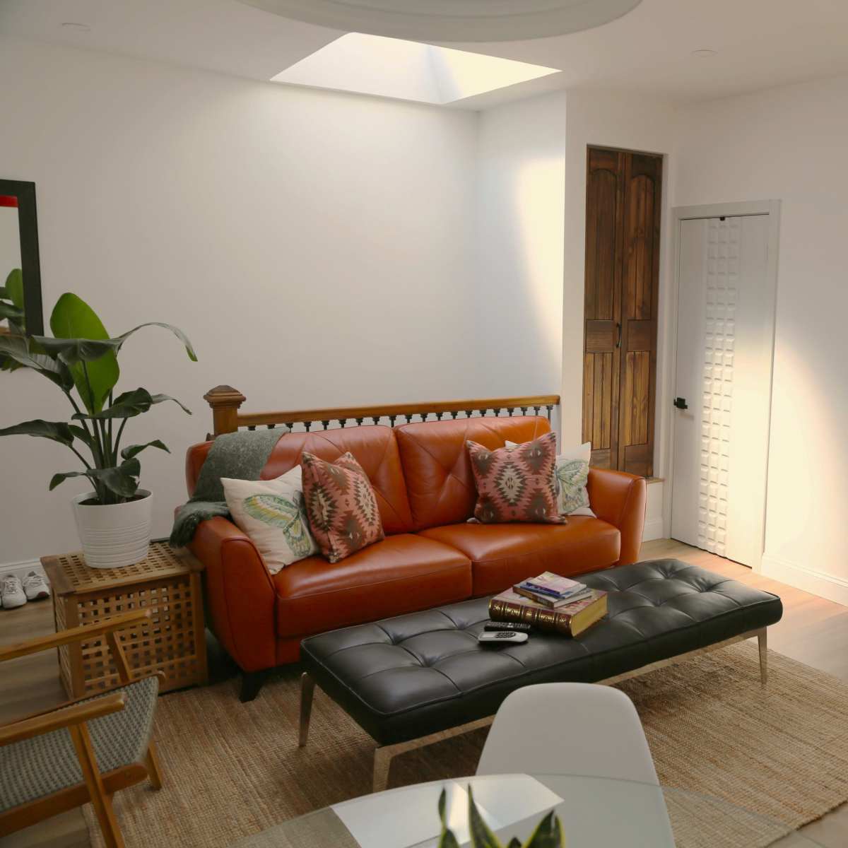 A modern living room features an orange leather sofa, a black coffee table, and a red accent chair, with two white doors and a skylight above.
