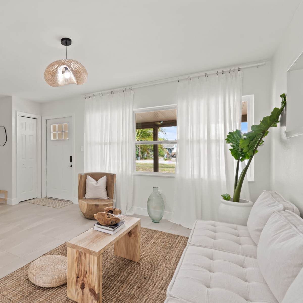 A light and airy living room featuring a white sofa, a wooden coffee table, and large windows with sheer curtains.