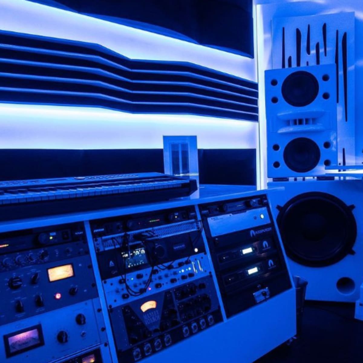 A modern music studio with a keyboard, audio equipment, and blue LED lighting.