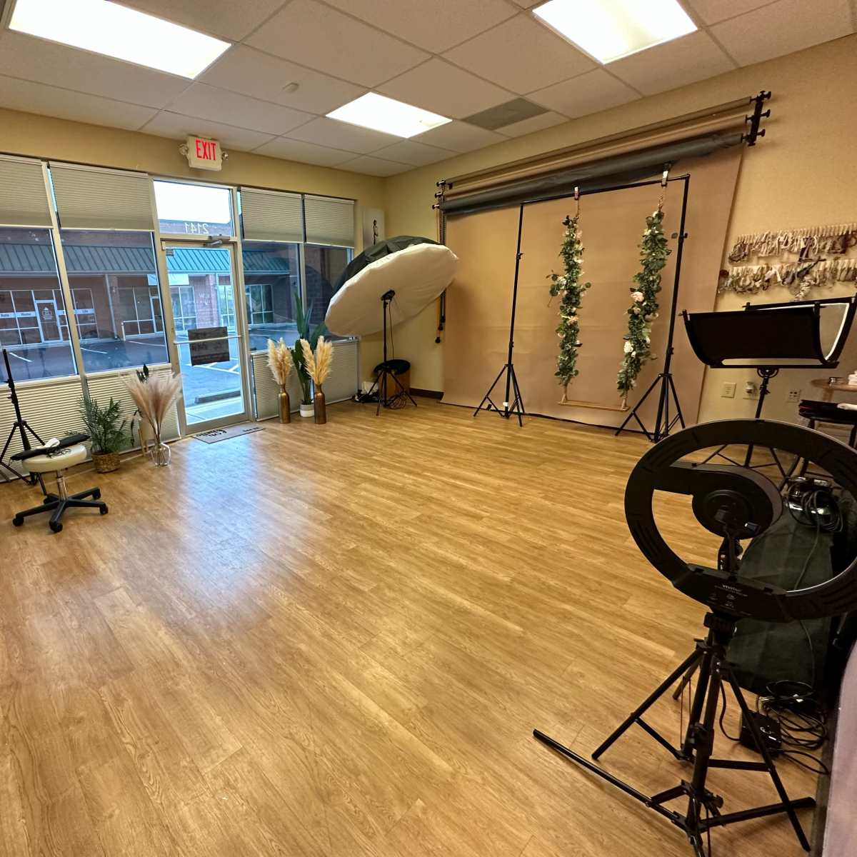An empty studio space with wooden flooring, a large window, and various photo equipment arranged along the walls.