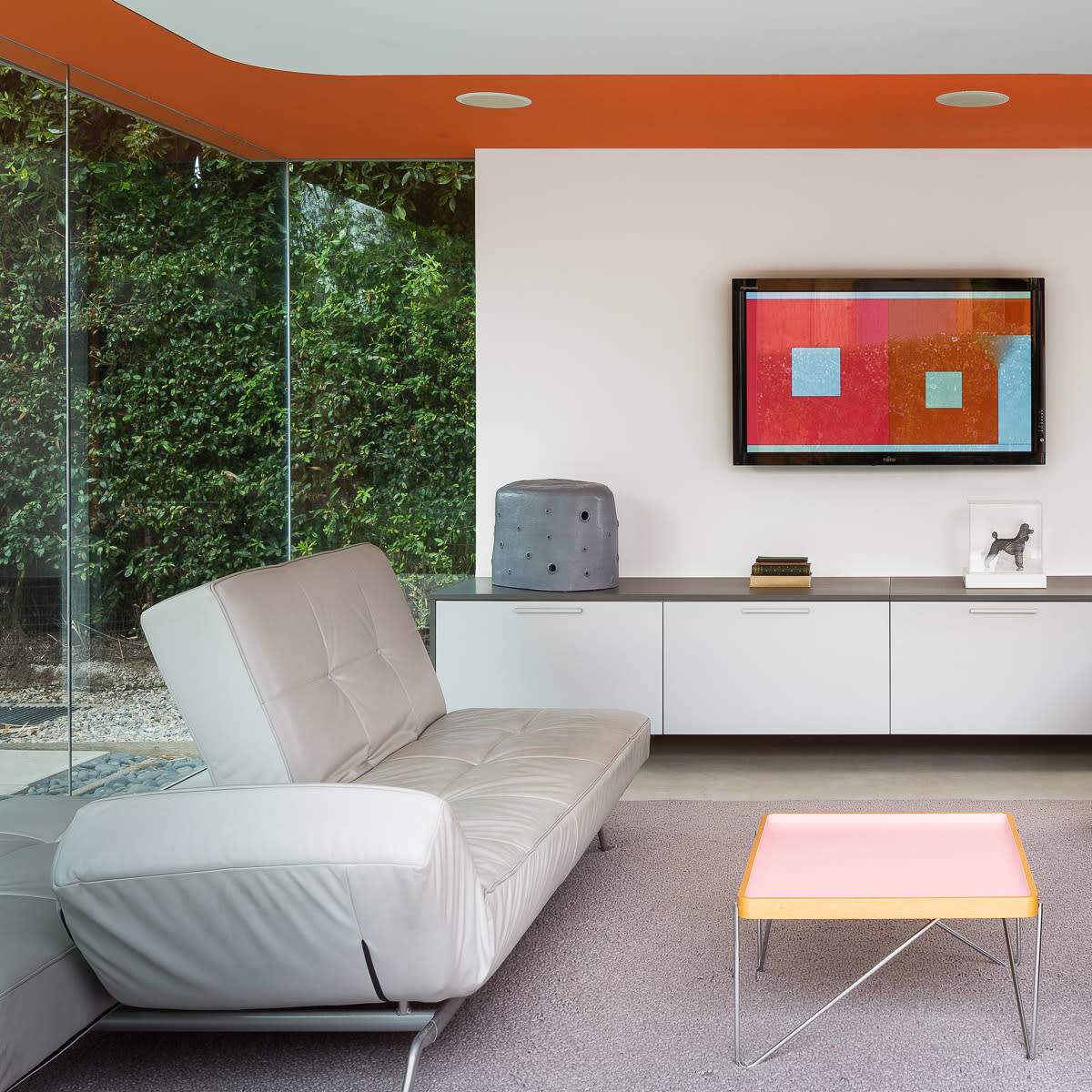 A modern living room features a white sofa, a gray armchair, and a pink coffee table, with a television mounted on the wall above a sleek console.
