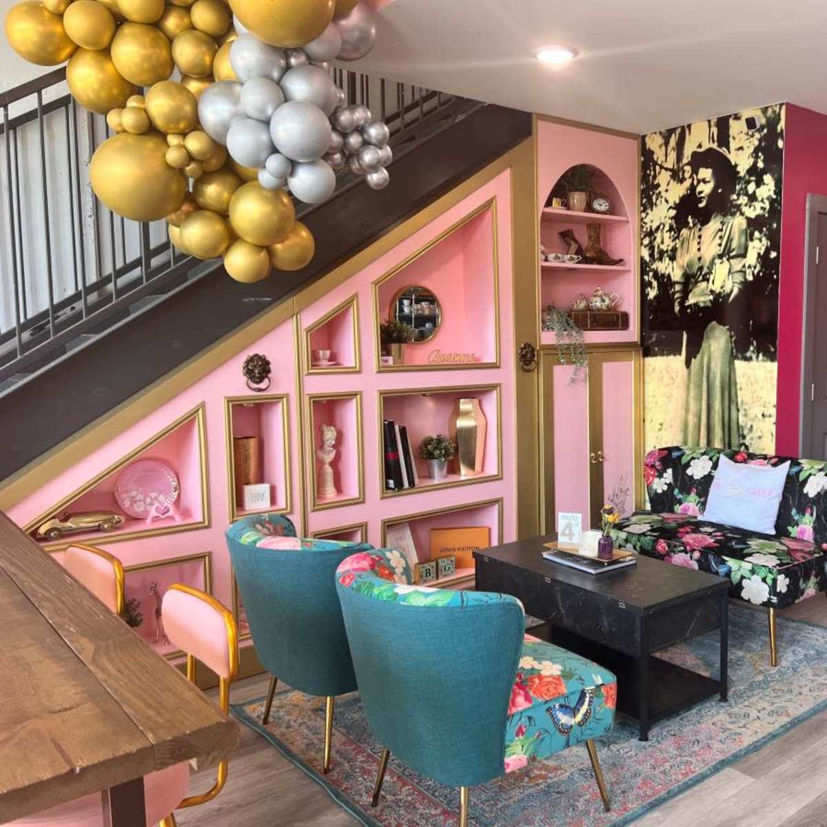A stylish interior space with colorful decor, featuring a seating area with patterned chairs, a black coffee table, and a wall display of shelves and a large photograph.