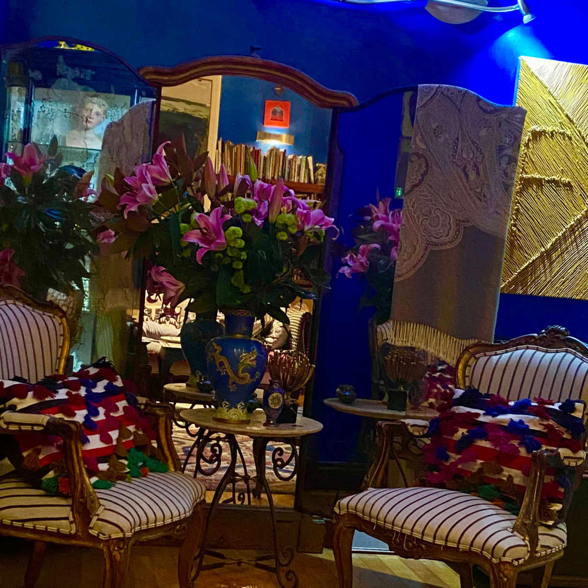 An elegantly styled room featuring two ornate chairs facing a small round table, adorned with vibrant flowers and a colorful area rug.
