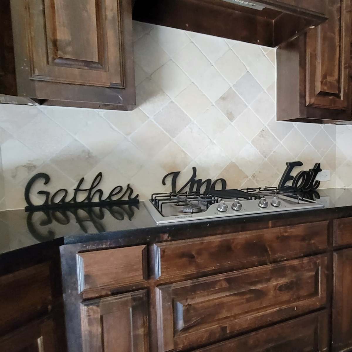 A kitchen with wooden cabinets, a gas stovetop, a black countertop, and decorative items on the counter.