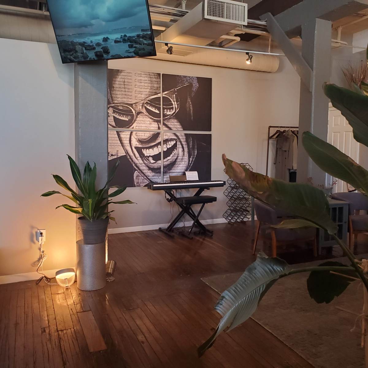 An interior space featuring a large mural of a smiling face, a piano, and plants, with seating arranged around the area.