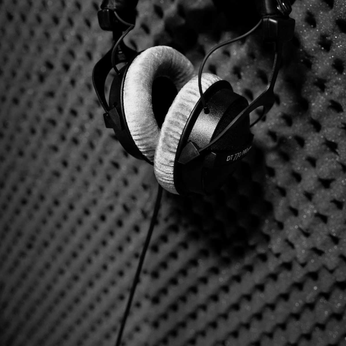 A pair of black headphones hangs against a textured soundproof wall.