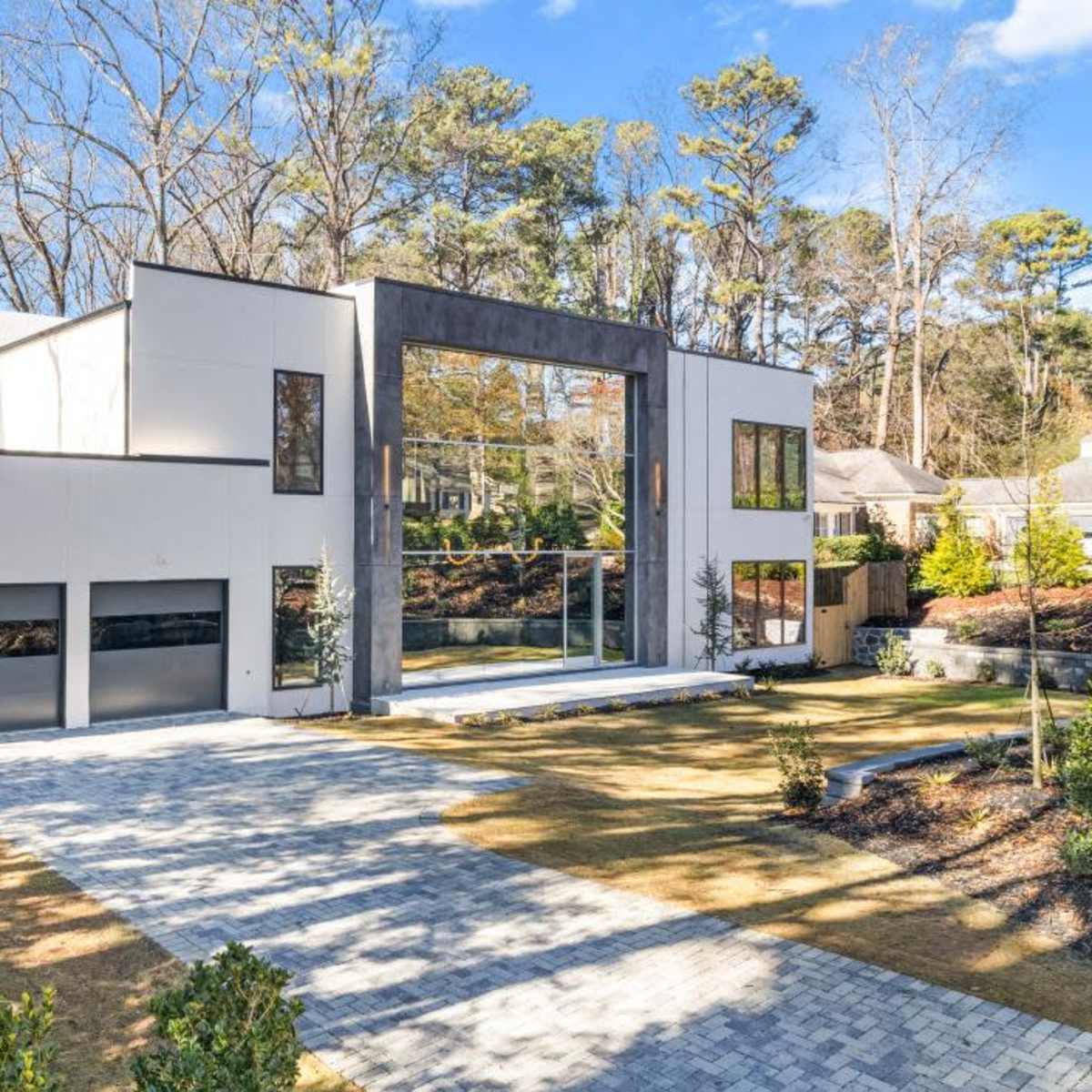 A modern two-story house with large glass windows and a three-car garage, surrounded by a landscaped yard.