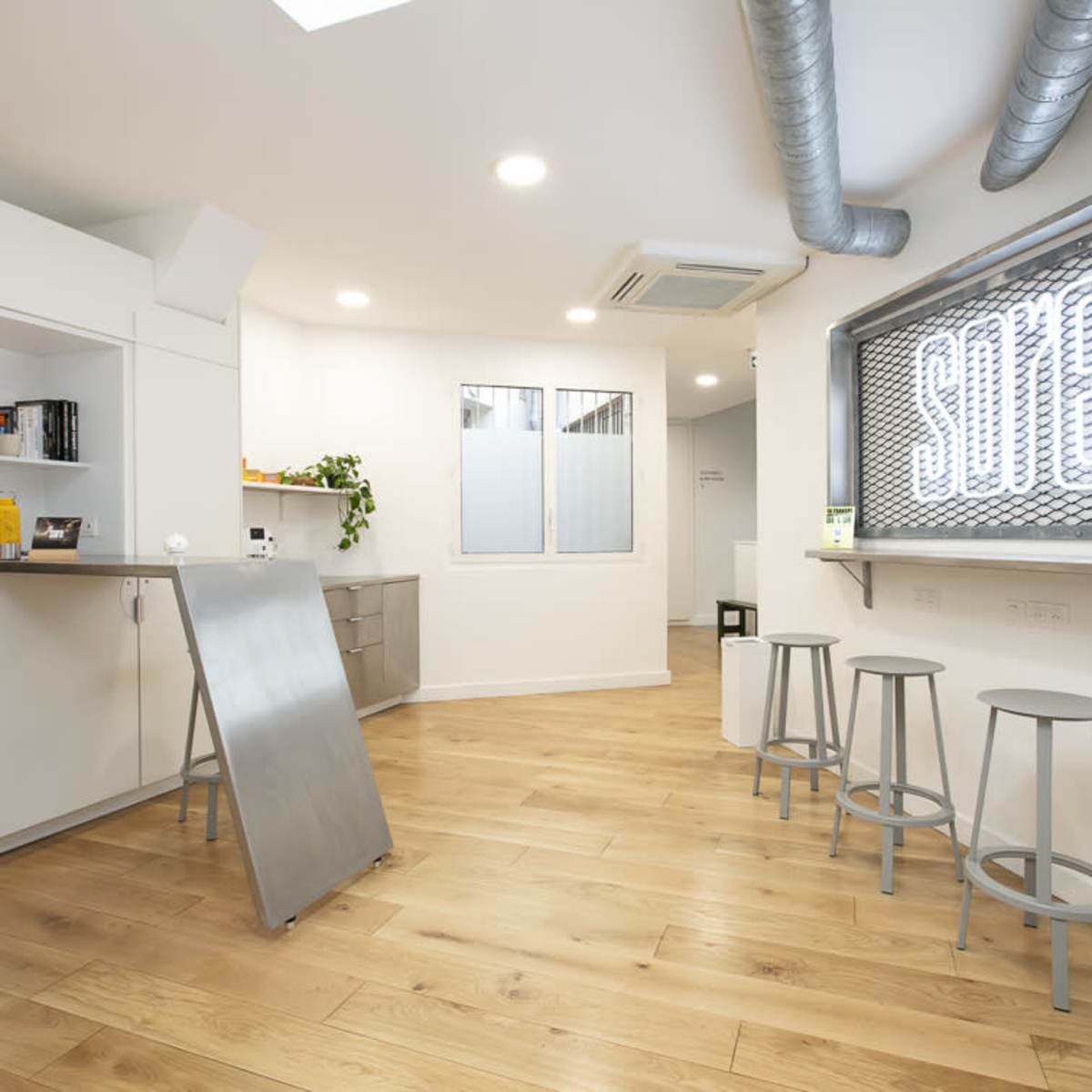 A modern interior space with light wood flooring, white walls, and a bar area with three metal stools.