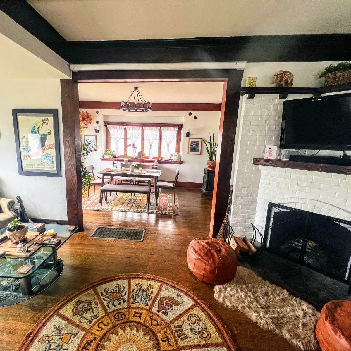 A cozy living room with a glass coffee table, a sectional sofa, and a view of a dining area through an open archway, featuring a fireplace and various decorations.