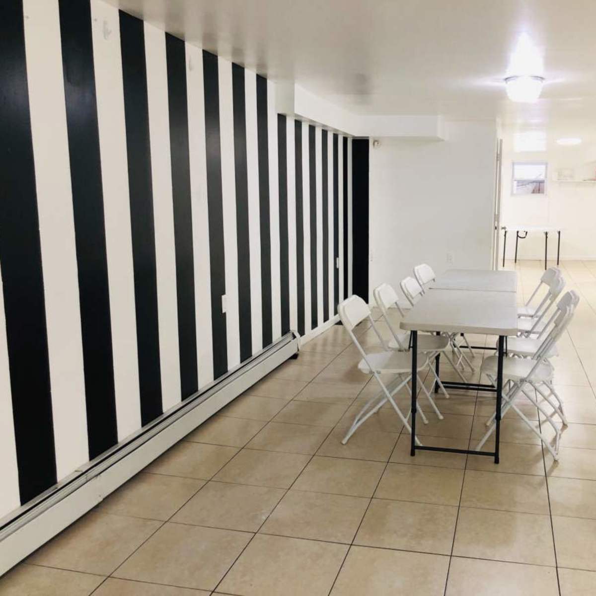 A room with a tiled floor, black and white striped walls, and a rectangular table surrounded by six folding chairs.