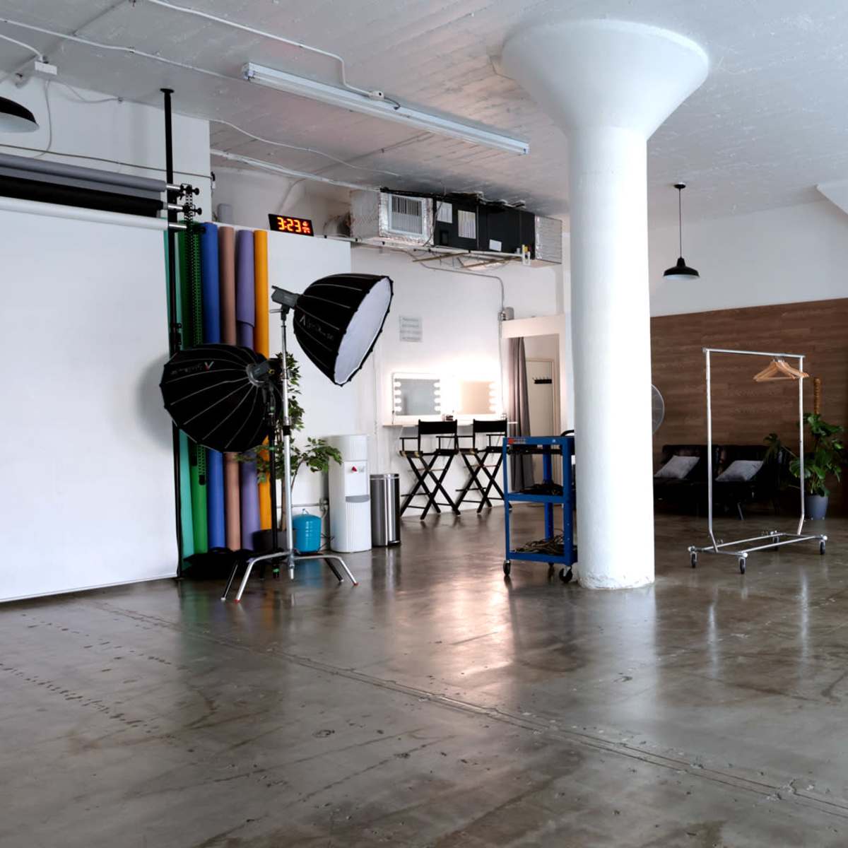 A spacious studio with a photography backdrop, lighting equipment, a mirror, and a clothing rack.