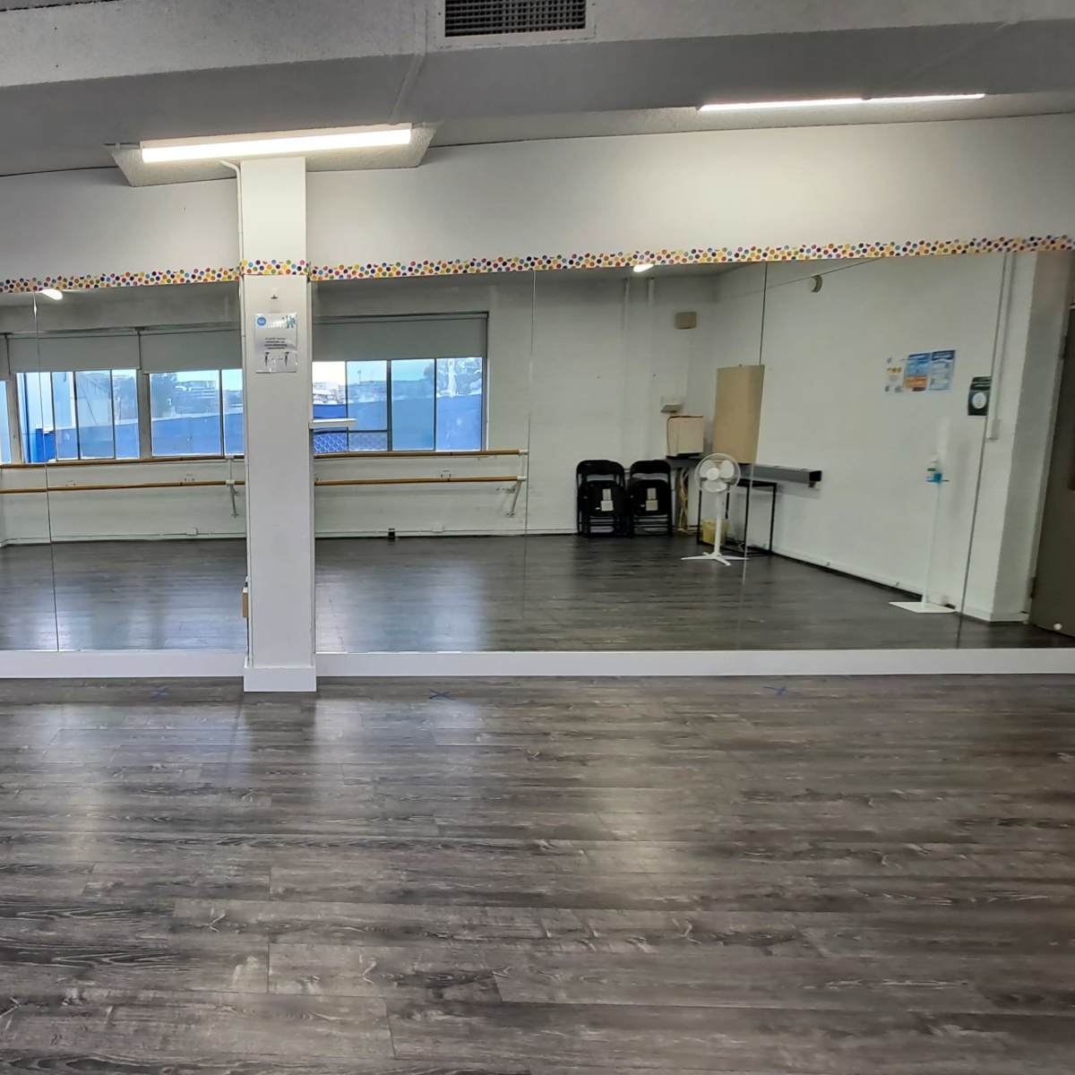 A spacious dance studio with a large mirrored wall, wooden ballet barres, and natural light coming through the windows.