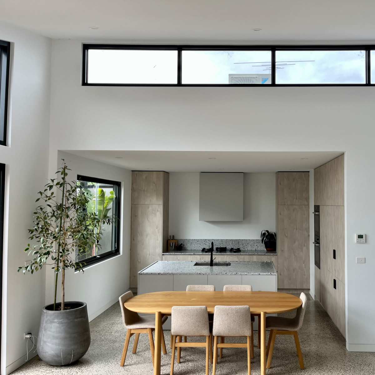 A modern kitchen and dining area features a sleek table with four chairs, large windows, and minimalist cabinetry.