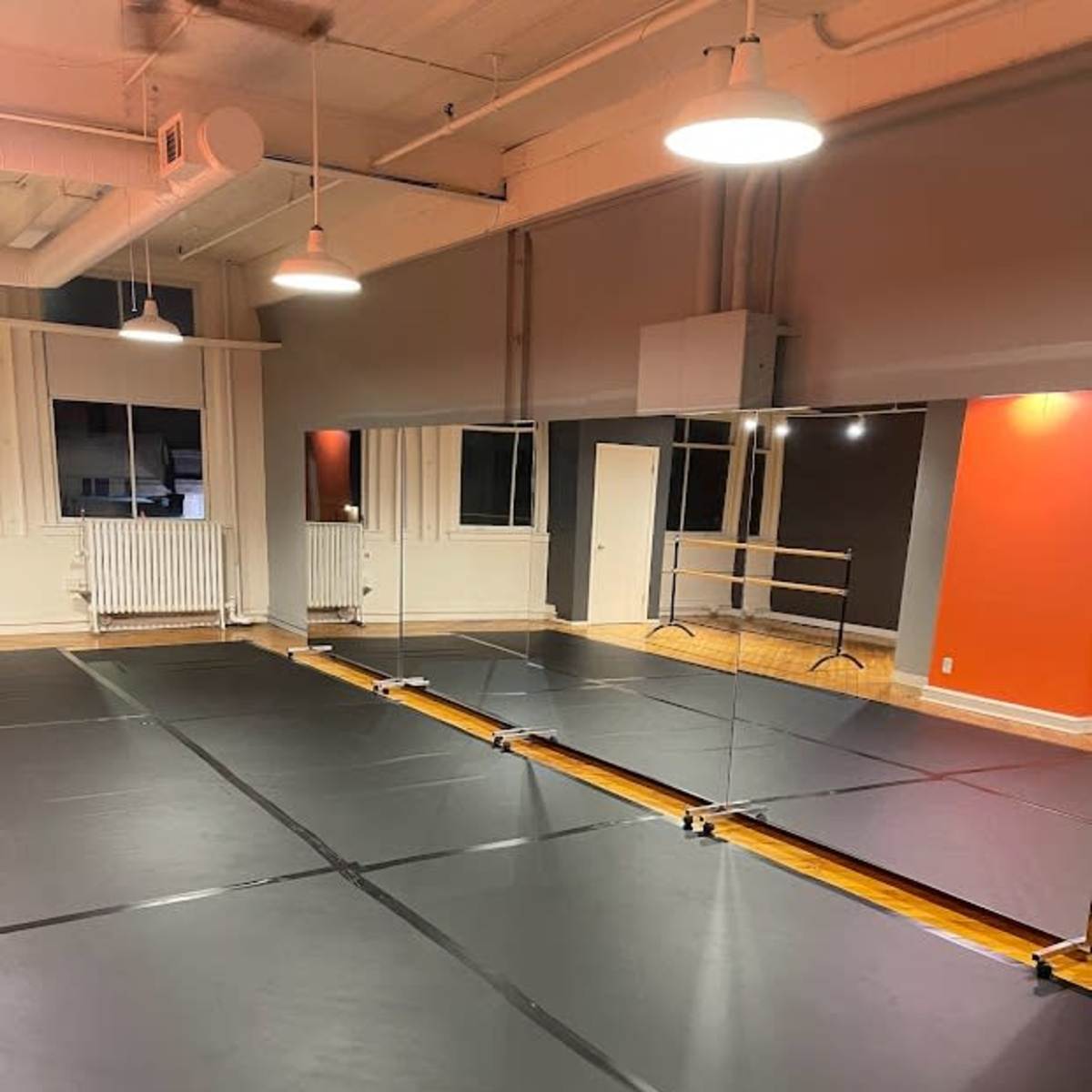 A dance studio with a large mirrored wall and a black rubber floor.