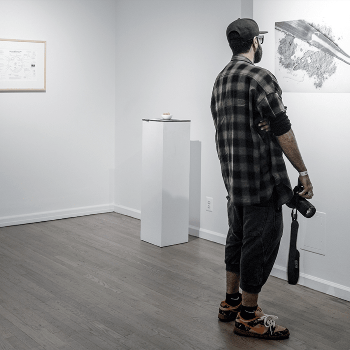 A man stands in an art gallery, observing a large black-and-white photograph of a whale displayed on the wall.