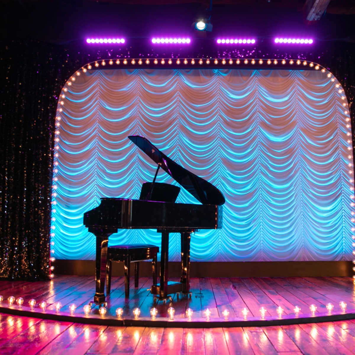 A grand piano sits on a circular stage adorned with lights and a draped backdrop.
