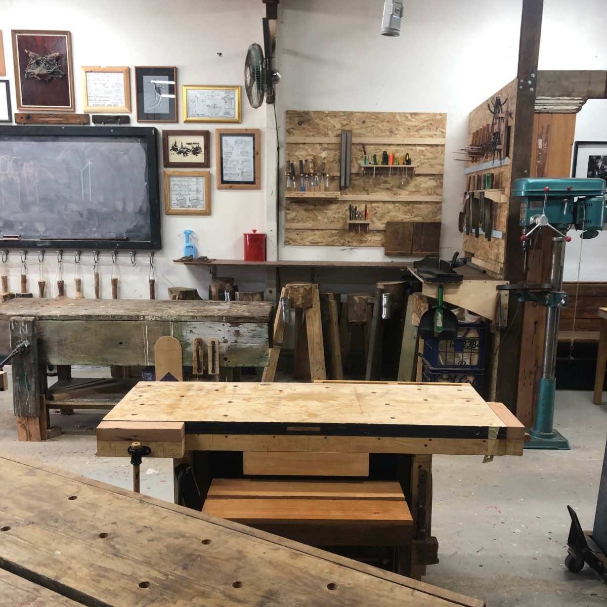 A woodworking shop with wooden workbenches, tools hanging on the walls, and a variety of equipment arranged in a functional layout.