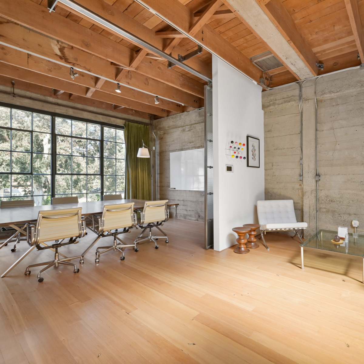 A modern office space with large windows, wooden beams, and a minimalist design featuring a glass coffee table and white furniture.