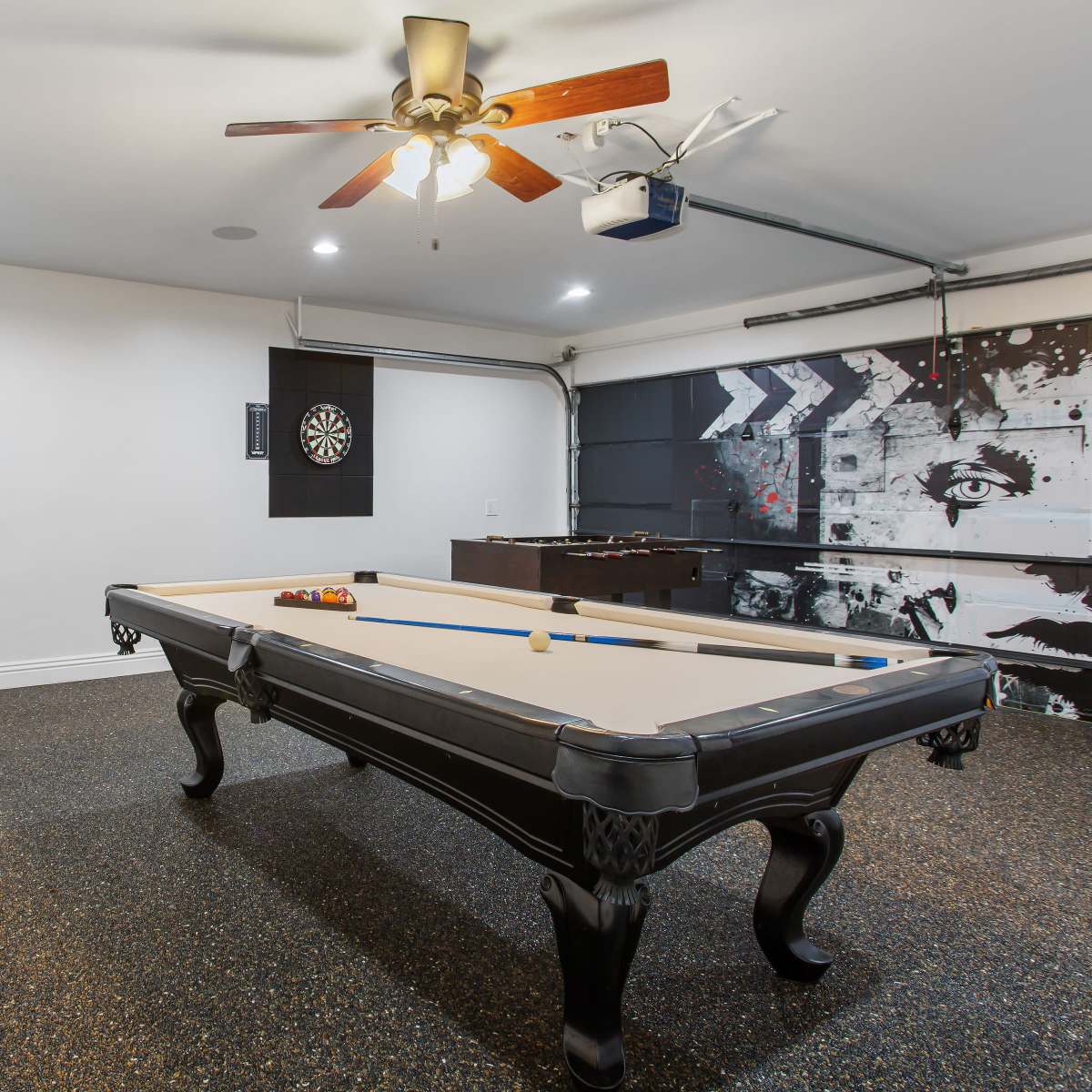 A game room features a pool table, a dartboard on the wall, and a foosball table in the corner.