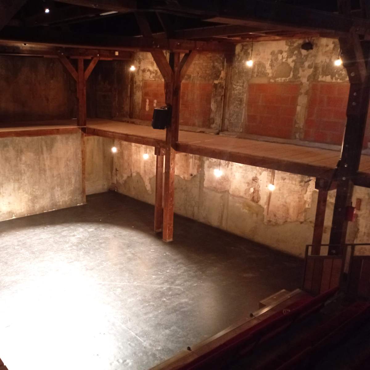 A circular, multi-level performance space with rustic wooden beams and a dimly lit floor.